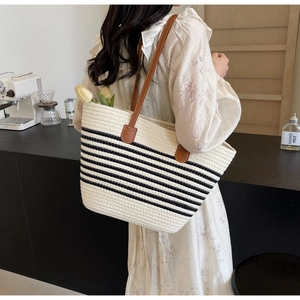 Detail of woven rope tote bag with black stripes and brown leather shoulder strap on shoulder