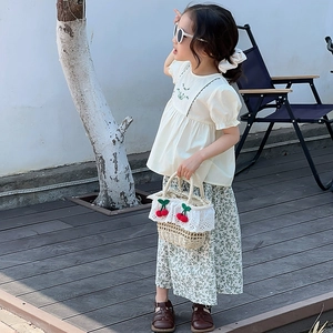 Detail of a straw tote bag with cherry accents and floral lace trim for kids