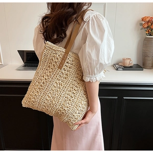 Close-up of beige woven straw tote bag with brown leather handles and reinforced stitching