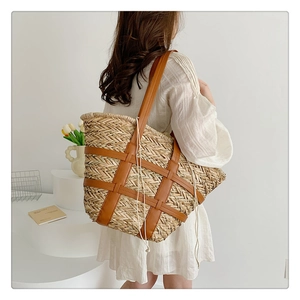Detail of a large woven straw tote bag with brown leather straps on a model in a white studio