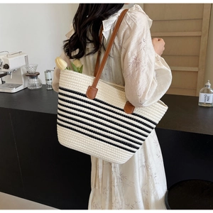 Detail of woven beige tote bag with black stripes and brown leather handles in a cafe