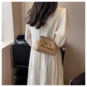 Détail d'un sac bandoulière en paille tressée beige avec fermoir baiser doré et broderie