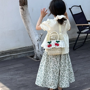 Detailed view of children's straw bag with cherry charm and lace on a small girl