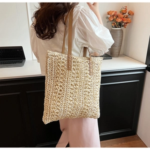 Detail of handwoven beige straw tote bag with brown leather handles and reinforced stitching