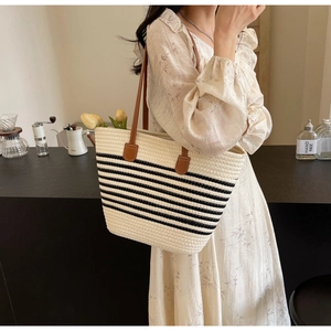 Detail view of woven tote bag with black stripes and brown leather shoulder straps