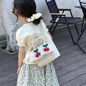 Outdoor view of girl carrying straw crossbody bag with white lace and cherry decoration