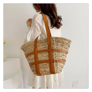 Detail of a straw woven tote bag with brown leather accents and white drawstring closure