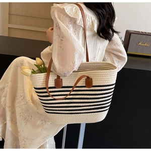 Detail of woven straw tote bag with black stripes and brown leather shoulder straps