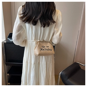 Détail d'un sac bandoulière en paille beige avec broderie Go on Holiday et chaîne dorée