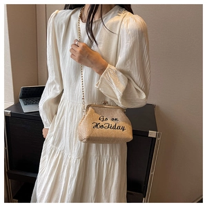 Détail du sac à main en paille tressée avec broderie Go on Holiday et chaîne dorée