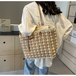 Détail du grand sac cabas en paille avec bandoulière en cuir marron porté par le mannequin