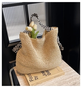 Détail d'un sac seau en paille beige avec bandoulière rayée et tulipes décoratives