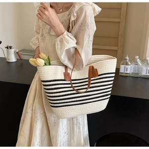 Detail of striped woven tote bag with brown leather handles worn by a model in casual setting