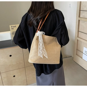 Détail d'un sac cabas en paille tissé à la main avec nœud en dentelle blanche et anse en cuir