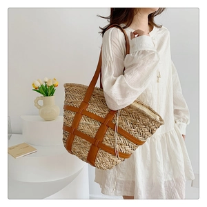 Detail of a large straw woven tote bag featuring brown leather straps and a drawstring liner