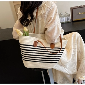 Detail of woven tote bag with black stripes and brown leather straps in a lifestyle scene