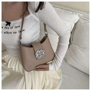 Detail of khaki PU leather handbag with oversized rhinestone buckle on model shoulder