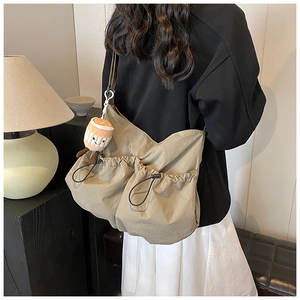 Detail view of khaki nylon messenger bag with two drawstring pockets and a plush pendant