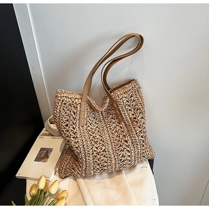 Minimalist straw tote bag with brown leather straps on a white fabric surface