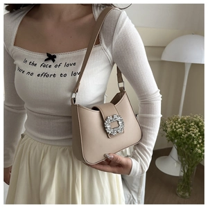 Detail of elegant beige crescent shoulder bag featuring a large sparkling rhinestone buckle
