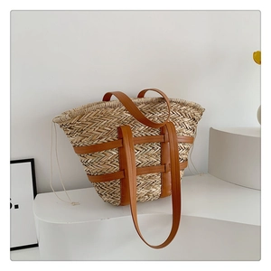 Minimalist straw tote bag with brown leather straps displayed on white studio platform