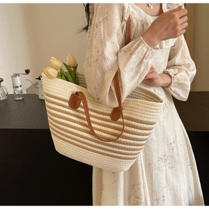 Detail of woven tote bag featuring brown leather handles and a textured striped pattern