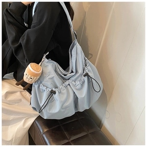 Detail of light blue drawstring tote bag with plush charm on a model's shoulder