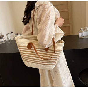 Detail of a beige woven tote bag with dark stripes and brown leather shoulder straps