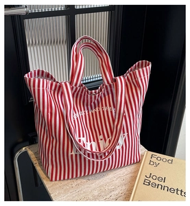 Detail of red and white striped canvas tote bag with Enjoy text on marble surface