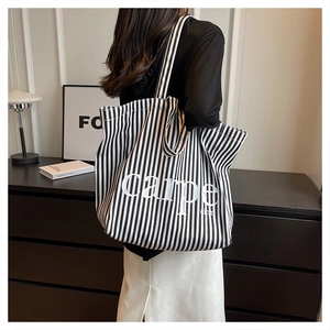 Detailed view of striped canvas tote bag with Carpe Diem text worn on shoulder