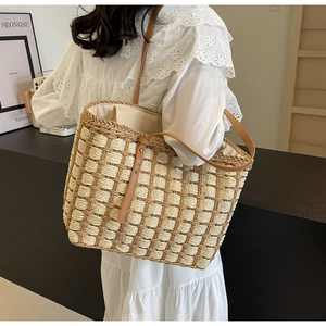 Détail d'un sac cabas en paille tressée avec anses en cuir marron et motif en treillis beige