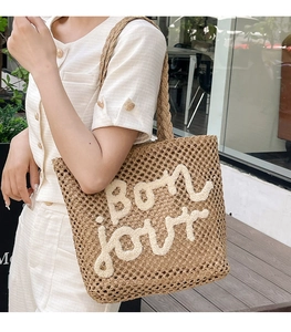 Detail of woven straw tote bag featuring white Bon jour textured embroidery