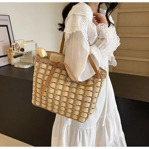 Détail du sac cabas en paille tissée avec anses en cuir marron porté de profil par un mannequin