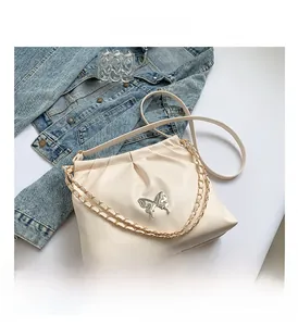 Close-up of the elegant silver butterfly buckle and pleat detail on a cream PU shoulder bag