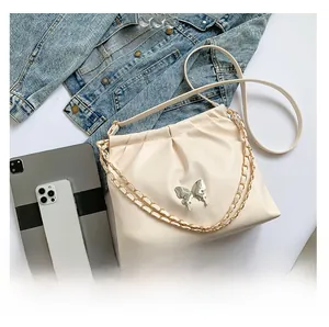 Detail of cream pleated cloud bag featuring silver butterfly charm and chain strap