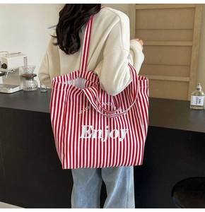 Detail of red and white striped canvas tote bag with Enjoy print in a cozy cafe setting