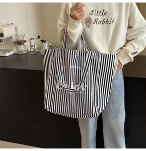 Close-up of stylish black and white striped canvas tote bag with Enjoy slogan in a cafe setting