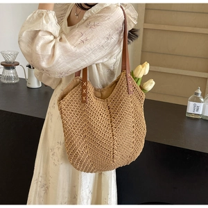Detail of straw woven tote bag featuring brown leather handle with X-shaped stitching