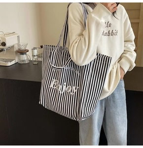 Detailed view of canvas tote bag with black and white vertical stripes and Enjoy text