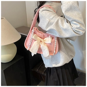 Close-up of pink corduroy shoulder bag featuring a white satin bow and woven straps