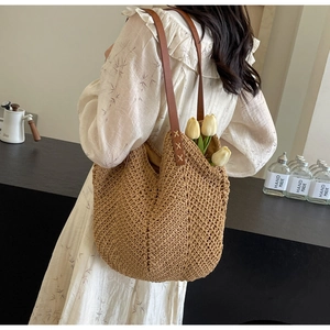 Detail of woven straw tote bag featuring brown leather strap and contrast stitching