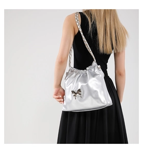 Close-up of metallic silver PU crossbody bag with a decorative metal bow and chain strap