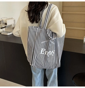 Detail view of stylish striped canvas tote bag worn on shoulder by model in a cafe
