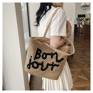 Detail of woven straw tote bag with black Bonjour embroidery and textured handles