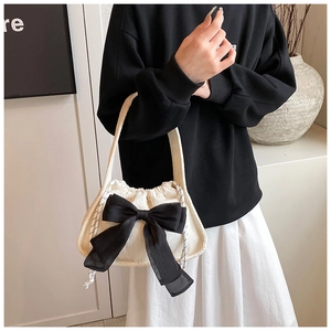 Detail of white corduroy handbag featuring a large black bow and drawstring closure