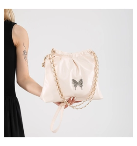 Detail of light beige pleated handbag featuring a silver metal butterfly buckle and gold chain