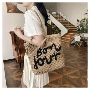 Detail of hand-woven straw tote bag with black bon jour embroidery and rope handles