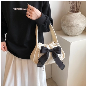Close-up of beige corduroy handbag featuring a large black bow and drawstring closure