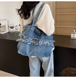 Détail du sac cabas en jean bleu avec des franges et une broderie de lettres blanches