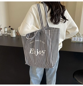 Rear view of model wearing a large black and white striped canvas tote bag with Enjoy print